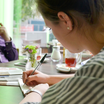Eine weibliche Person schreibt in einem Café etwas in ein Notizbuch