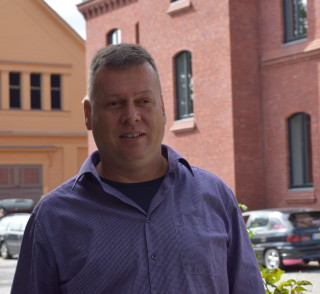 Stadtverordneter Uwe Fröhlich (Bündnis 90/ Die Grünen) steht vor einem roten Backsteingebäude und berichtet über Fairtrade-Towns. Foto: Lilith Grull