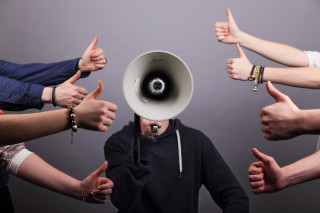 Einem Menschen mit Megaphon werden positive Daumen entgegen gestreckt
