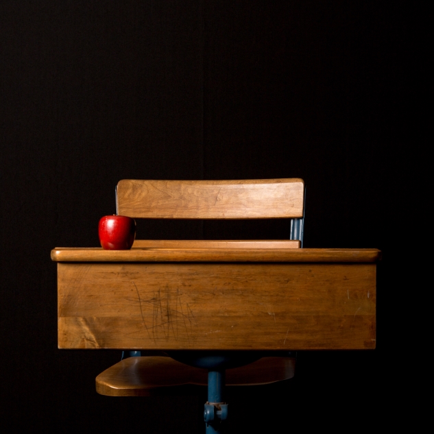 Eine hölzerne Schulbank vor schwarzem Hintergrund mit Apfel