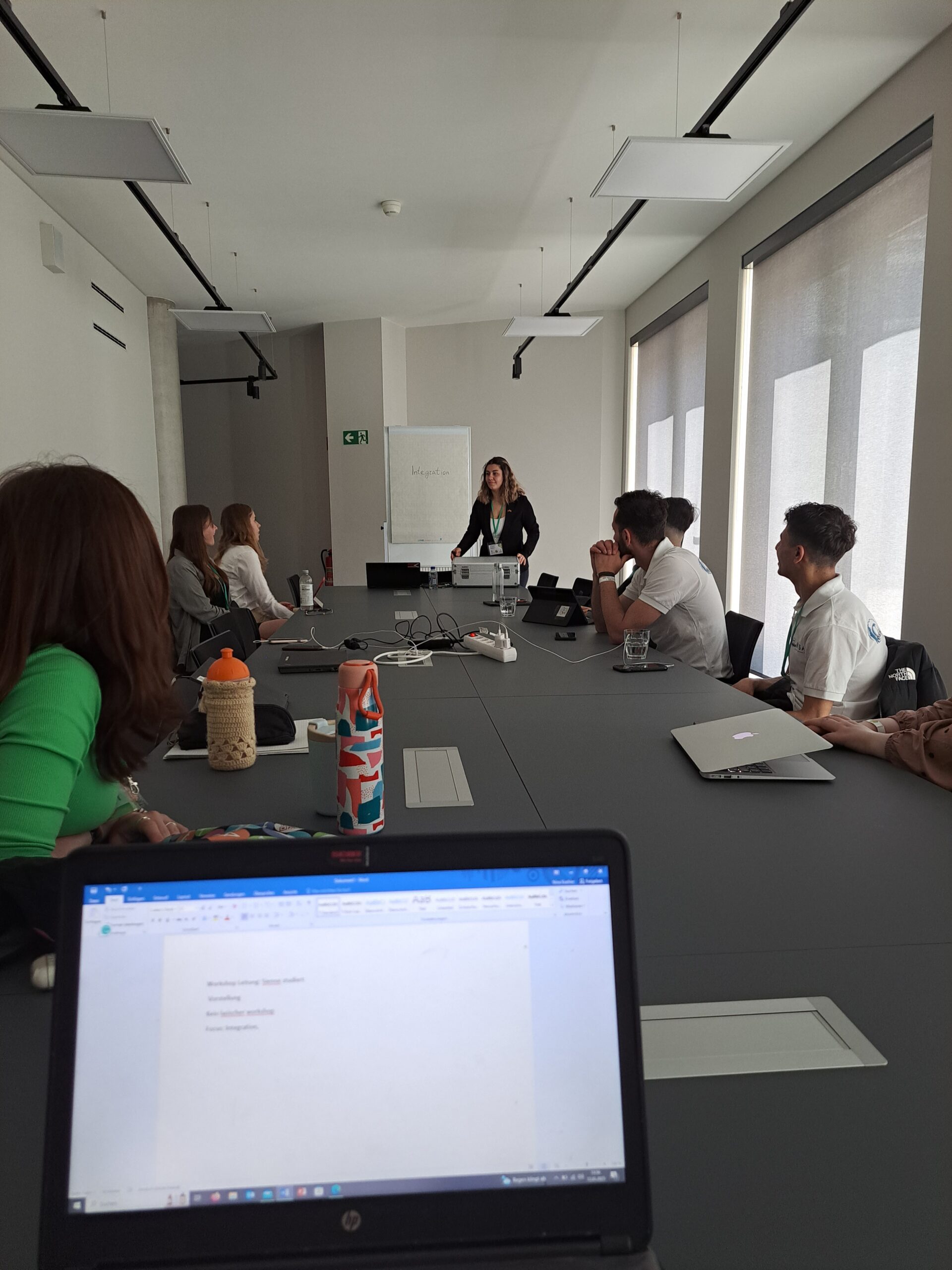 8 Personen ihn einem Konferenzraum, eine Person steht vor einem Writeboard